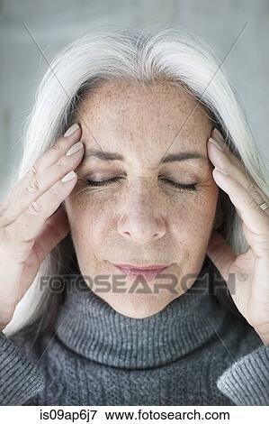 Stock Photo - Close up of mature woman meditating with eyes closed and hands on forehead. Fotosearch