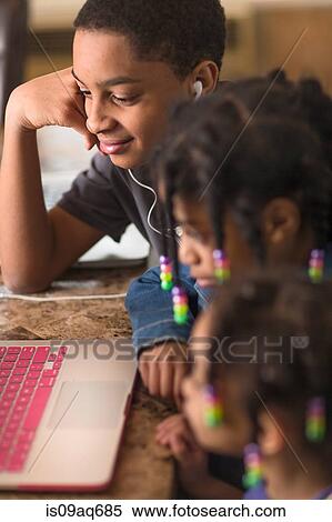 Stock Photography - Close up of teenage boy and sisters at dining table using laptop. Fotosearch