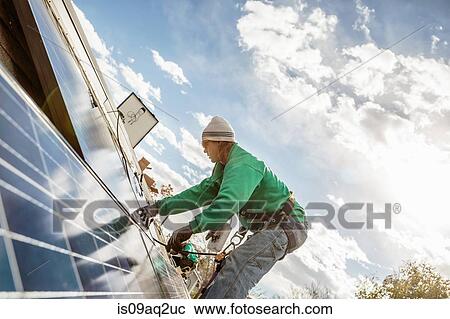 Stock Image - Construction crew member installing a solar panel on a house. Fotosearch