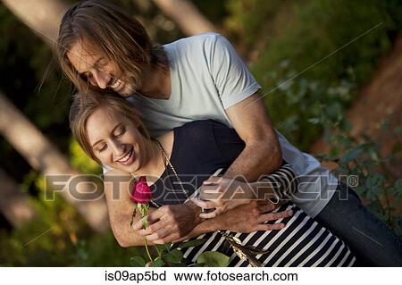 Stock Image - "Couple hugging, woman holding rose". Fotosearch