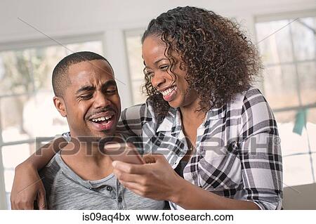 Stock Photo - Couple reading and laughing at texts on smartphone. Fotosearch