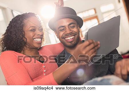 Picture - Couple sitting on sofa looking at digital tablet. Fotosearch
