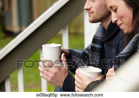 Stock Photography - Cropped shot of young couple sitting on porch step drinking coffee. Fotosearch