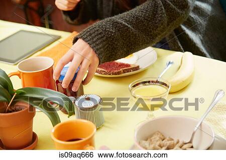 Stock Photograph - Cropped shot of young womans hands holding jam jar at breakfast table. Fotosearch