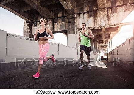 Stock Photo - Female and male runners running under city bridge. Fotosearch