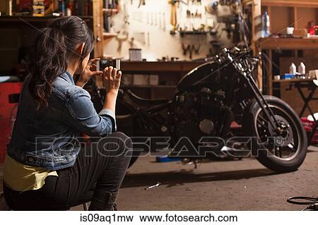 "Female mechanic in workshop, taking photograph of motorcycle using smartphone" View Large Photo Image Stock Photo - "Female mechanic in workshop, taking photograph of motorcycle using smartphone". Fotosearch