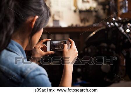 "Female mechanic in workshop, taking photograph of motorcycle using smartphone" View Large Photo Image Stock Photo - "Female mechanic in workshop, taking photograph of motorcycle using smartphone". Fotosearch