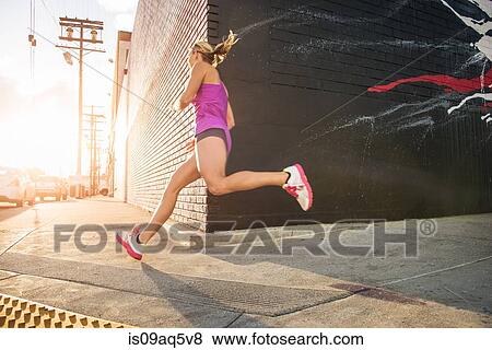 Stock Photo - Female runner running along sidewalk. Fotosearch