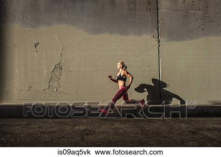 Stock Image - Female runner running on sidewalk. Fotosearch