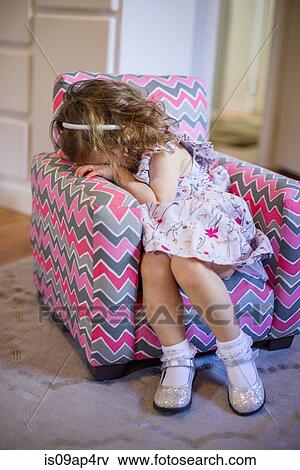 Stock Photo - Female toddler with hiding her face on childs armchair. Fotosearch