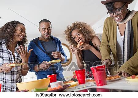 Stock Photography - Four adult friends chatting and eating party food in kitchen. Fotosearch