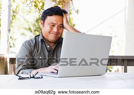 Stock Image - Frustrated mature businessman working on laptop in porch. Fotosearch