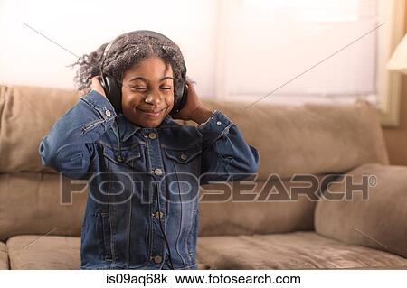 Stock Image - Girl with eyes closed listening to headphone music on sofa. Fotosearch