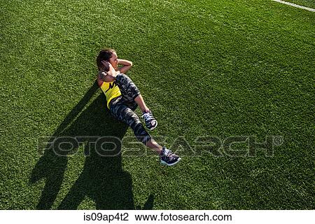 Stock Image - High angle view of young female athlete doing sit ups on sports field. Fotosearch