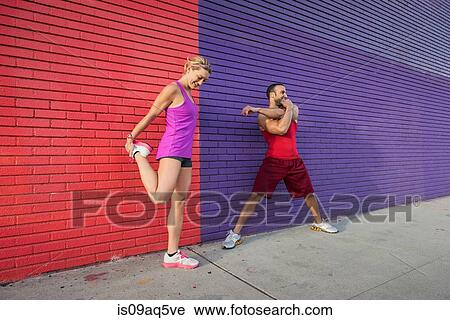 Stock Image - Male and female runners warming up on sidewalk. Fotosearch