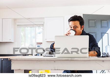 Mature businessman typing on laptop whist drinking takeaway coffee at kitchen table View Large Photo Image Stock Image - Mature businessman typing on laptop whist drinking takeaway coffee at kitchen table. Fotosearch