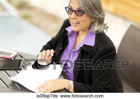"Mature businesswoman sitting at table, going through document" View Large Photo Image Stock Photograph - "Mature businesswoman sitting at table, going through document". Fotosearch