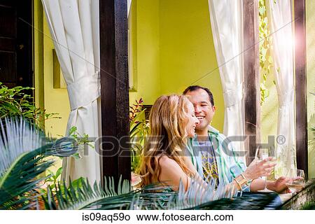 Picture - Mature couple sitting drinking white wine in garden porch. Fotosearch