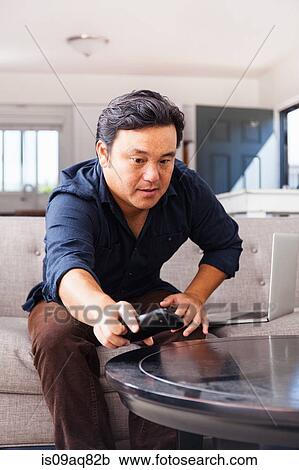 Stock Image - Mature man on sofa reaching for remote control. Fotosearch