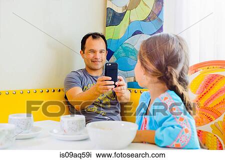 Mature man photographing daughter on smartphone View Large Photo Image Stock Image - Mature man photographing daughter on smartphone. Fotosearch