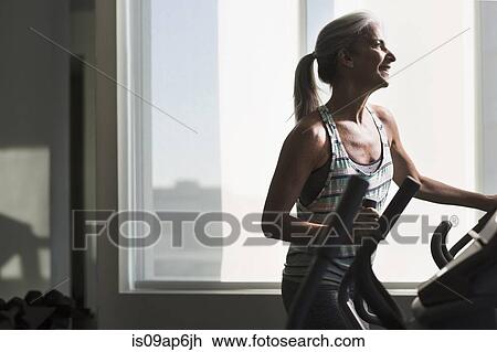 Stock Image - Mature woman exercising on gym machine. Fotosearch