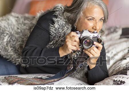 "Mature woman relaxing on bed, holding SLR camera" View Large Photo Image Stock Photo - "Mature woman relaxing on bed, holding SLR camera". Fotosearch