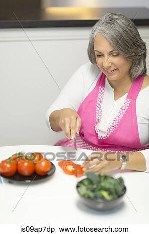 Mature woman slicing tomatoes at table View Large Photo Image Stock Photography - Mature woman slicing tomatoes at table. Fotosearch