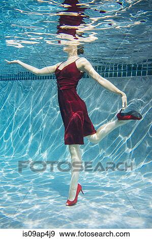 Stock Photo - "Mature woman wearing red dress and high heels, standing on one leg, underwater view". Fotosearch