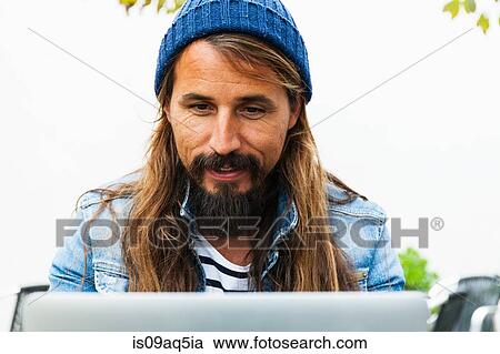 Mid adult man wearing hat using laptop View Large Photo Image Stock Image - Mid adult man wearing hat using laptop. Fotosearch