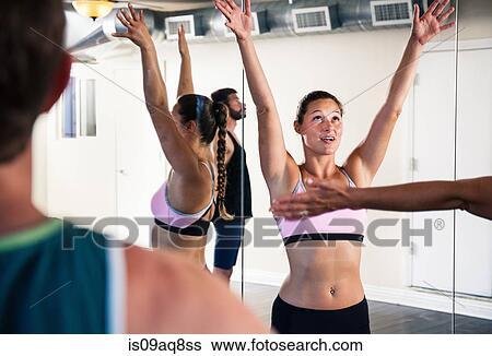 Stock Photograph - Mid adult woman in yoga class with arms raised. Fotosearch