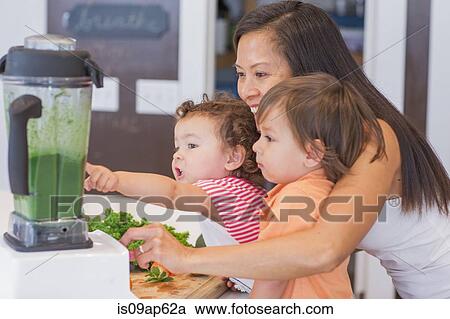 Mid adult woman making green smoothie for two toddlers in kitchen View Large Photo Image Stock Image - Mid adult woman making green smoothie for two toddlers in kitchen. Fotosearch