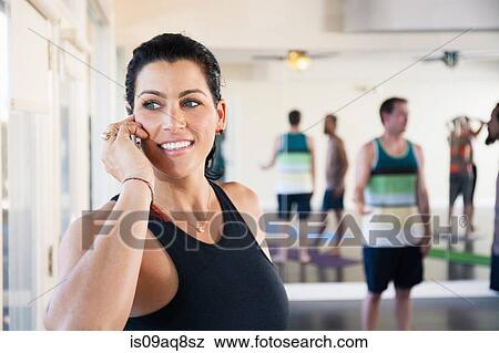 Stock Photo - Mid adult woman on cell phone in exercise studio. Fotosearch