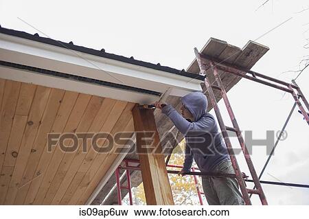 Stock Photo - Mid adult woman painting varnish on wood outside house. Fotosearch
