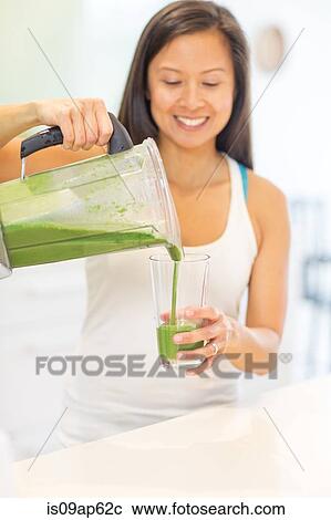 Mid adult woman pouring green smoothie in kitchen View Large Photo Image Stock Image - Mid adult woman pouring green smoothie in kitchen. Fotosearch