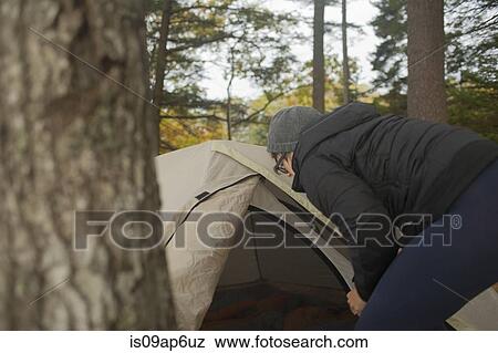 Stock Photo - "Mid adult woman preparing tent in forest, Maine, USA". Fotosearch