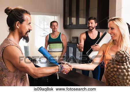 Stock Image - Mid adult woman shaking hands with yoga instructor. Fotosearch