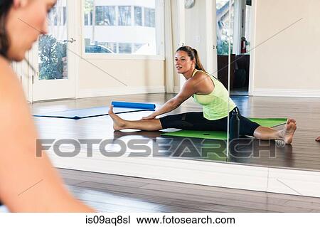Stock Image - Mid adult woman stretching in front of mirror. Fotosearch