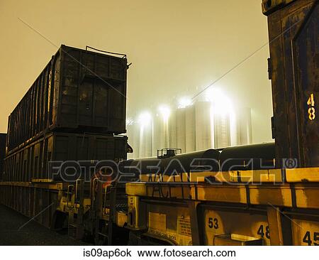 Stock Image - "Misty view of industrial storage tanks between freight locomotive at night, Seattle, Washington, USA". Fotosearch