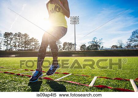 Stock Photography - Neck down view of female athlete training with agility ladder on sports field. Fotosearch