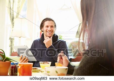 Stock Image - Over shoulder view of young man using digital tablet at breakfast table. Fotosearch