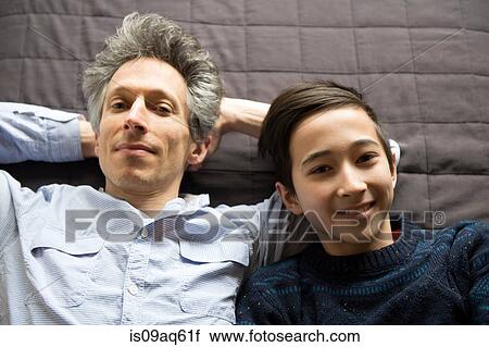 Stock Image - Overhead portrait of teenage boy and father lying back. Fotosearch