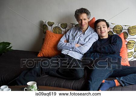 Stock Photo - Portrait of father and teenage son relaxing on sofa. Fotosearch