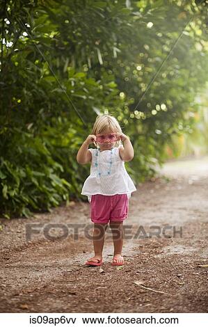 "Portrait of female toddler putting on pink sunglasses on woodland beach path, Anna Maria Island, Florida, USA" View Large Photo Image Stock Photo - "Portrait of female toddler putting on pink sunglasses on woodland beach path, Anna Maria Island, Florida, USA". Fotosearch