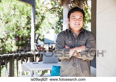 Stock Image - Portrait of mature man with arms folded on porch. Fotosearch