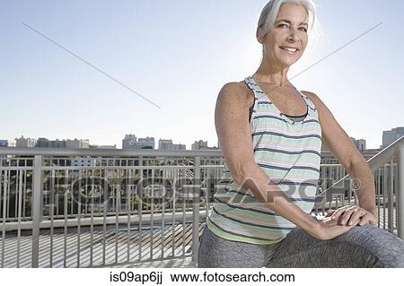 Stock Image - Portrait of mature woman doing warm up exercises on city balcony. Fotosearch