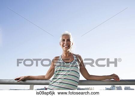 Portrait of mature woman in sports clothing leaning against city balcony View Large Photo Image Stock Image - Portrait of mature woman in sports clothing leaning against city balcony. Fotosearch
