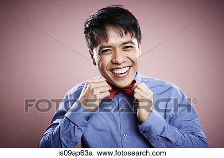Stock Image - "Portrait of mid adult man, adjusting bow tie, smiling". Fotosearch