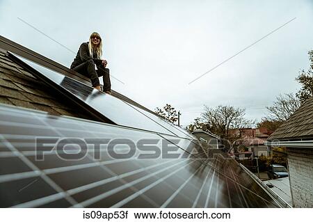 Stock Image - Portrait of mid adult woman sitting on newly solar paneled house roof. Fotosearch