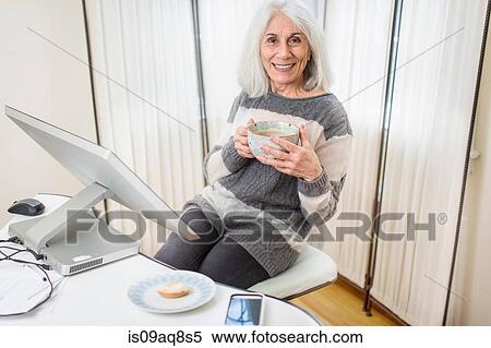 Portrait of senior woman sitting at computer holding cup View Large Photo Image Stock Photography - Portrait of senior woman sitting at computer holding cup. Fotosearch