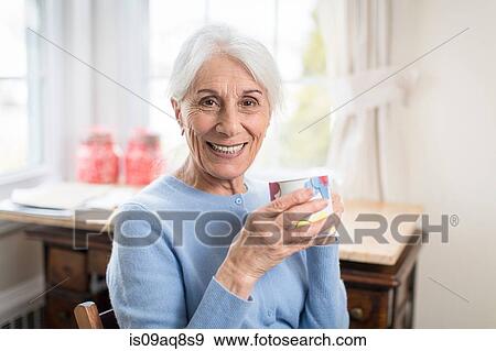 Portrait of smiling senior woman at home holding cup View Large Photo Image Stock Photo - Portrait of smiling senior woman at home holding cup. Fotosearch